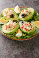 Fresh avocado stuffed with chicken salad on a bed of leafy greens close-up on a plate on the table. Vertical