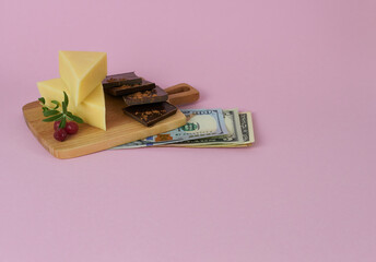 Hard cheese and chocolate cubes on a wooden plank with a wad of money. The concept is an economic...