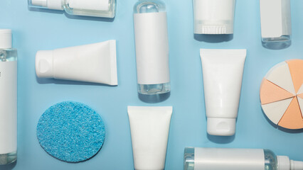 White natural cosmetic products, bottles and tubes with branding mockup on blue table background, top view, flat lay. Facial care and beauty