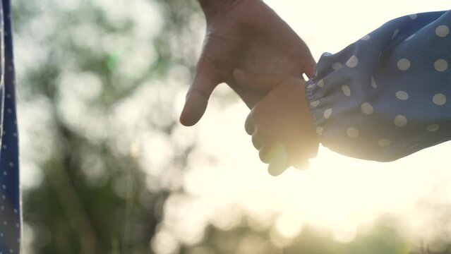 Happy family. Mom holds her daughter by hand. Family outdoors in the park. Mom in the natural forest holds the child by the hand. Happy daughter takes mom by the hand. People palms close-up. Sun rays