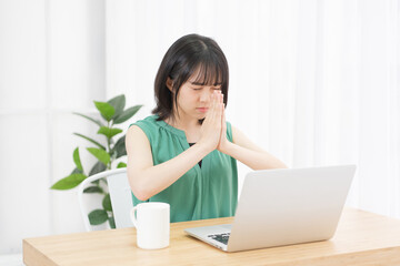 PCの前で手を合わせて祈っている若い女性