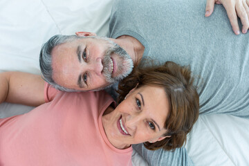 Caucasian senior older couple lying down on bed then look at each other. 