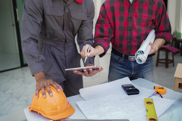 Smiling young architect or engineering builder in hard hat with tablet over group of builders at...