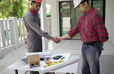 Smiling young architect or engineering builder in hard hat with tablet over group of builders at...