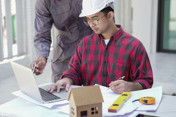 Smiling young architect or engineering builder in hard hat with tablet over group of builders at...