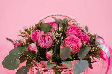 Bouquet of pink roses in a wicker basket on a pink table background. Birthday, Wedding, Mother's Day, Valentine's Day, Women's Day. Front view