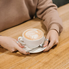 Woman hands holding a cup of hot cappuccino coffee in her hands.