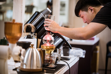 Professional coffee maker - Barista using coffee siphon brewing hot espresso at coffee shop coffee brewing syphon alternative method. Startup Business Concept.