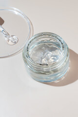 Jar with transparent cosmetic product, aloe gel or creamgel on beige pastel background. Liquid gel spilled out of cosmetic pipette on petri dish. Unbranded packaging, copy space.