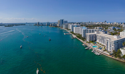 Fototapeta na wymiar Intracoastal buildings in an aerial view at Miami Beach, Florida. Waterfront with boats and harbors at the front of some buildings on the right side and background of clear blue skyline.