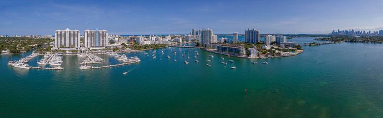 Panoramic view of intracoastal waterway in between modern high-rise buildings - Miami Beach, Florida. Waterfront houses with boats on the blue waterway and a blue sky background.