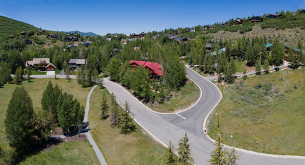 Mountain roads and beautiful houses against blue sky in Park City Utah. Nature landscape with homes on a residential neighborhood surrounded by lush foliage on a sunny day.