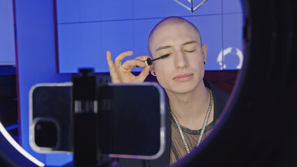 Caucasian gay man streaming online makeup video tutorial with mobile phone at home, medium closeup. High quality photo