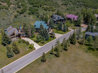 Aerial view of houses and roads amidst evergreen trees in Park City Utah. Beautiful homes on a residential neighborhood surrounded by lush nature scenery on a sunny day.