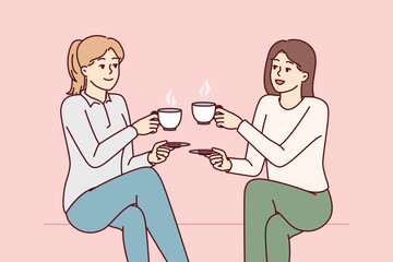 Two beauty girl friends drink hot coffee holding cups and saucers enjoy joint coffeebreak. Ladies dressed in casual style gossip during lunch break with hot non-drinks in hands - obrazy, fototapety, plakaty
