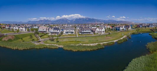 Beautiful houses in Daybreak Utah with view of river in the foreground. Magnificent mountains, blue sky, and clouds can be seen in the background of the neighborhood.