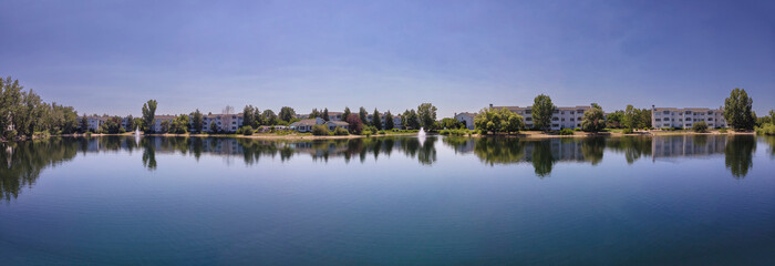 Panorama of small lake with reflections of apartments and trees under the purple sky in Boise, Idaho. There is a small lake at the front with reflection of purple sky above.