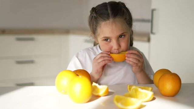 girl child eating oranges. happy family fruit healthy food kid concept. little girl daughter eating oranges at the table in the kitchen indoors. dream juicy fruits oranges are for a healthy diet