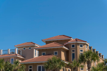 Fototapeta na wymiar Two large residential buildings with railings on roof decks in Destin, Florida. There are palm trees outside the mansions villas against the clear blue sky.