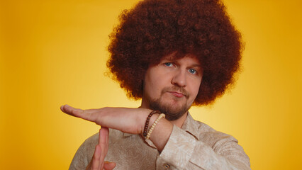 Tired serious upset bearded man with lush afro hairstyle coiffure showing time out gesture, limit or stop sign, no pressure, i need more time, break, pause. Hipster guy on yellow studio background