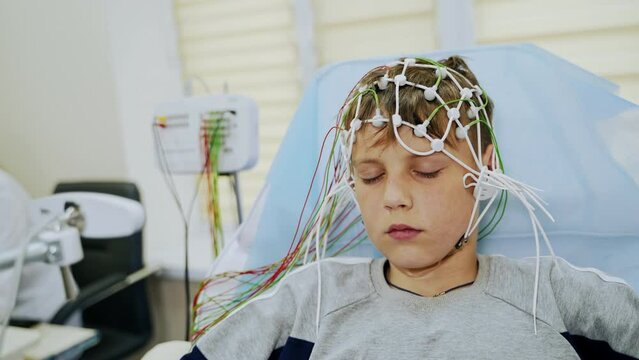 Teenager sits with his eyes closed undergoing EEG testing. Lots of sensors attached to the boy&rsquo;s head. Close up.