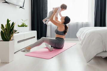 Young sporty mother and baby girl working out, exercising together at home, parent and child healthy development, game playing, fitness and relaxation,