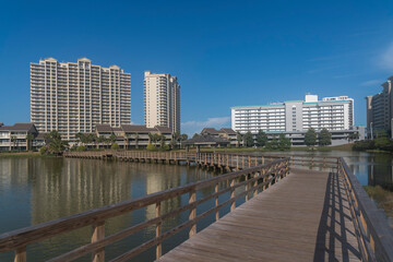 Fototapeta na wymiar Wooden boardwalk with railings with views of modern high rise buildings in Destin, Florida. Wooden walkway over the reflective water near the city buildings