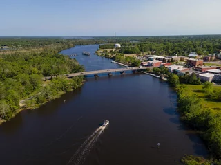 Foto op Plexiglas Wide river with passenger boat travelling under the bridges in Milton, Florida. River waterway in between the land areas with trees on left and buildings on the right connected by the bridges. © Jason