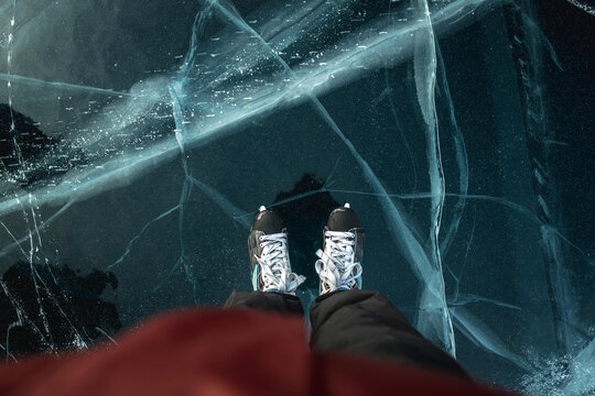 Feet in skates on the beautiful blue cracked ice of a frozen lake. View of the top