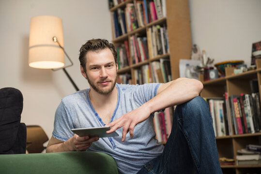 Mid adult man using digital tablet in living room, Munich, Bavaria, Germany
