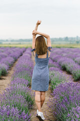 Girl standing back in a lavender flowers field. A beautiful woman walk on the lavender field. Enjoy the floral glade, summer nature. Natural cosmetics concept. Back view.