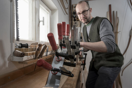 Male bow maker fixing wood in bow shape in workshop, Bavaria, Germany