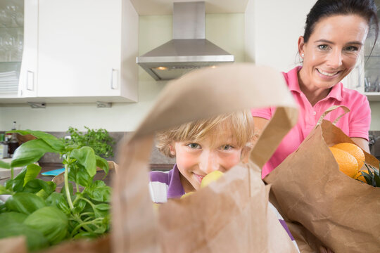 Boy Helping His Mother With Grocery Bags In Kitchen, Bavaria, Germany