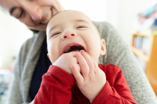Baby Boy Smiling and Chewing on His Fingers While Being Held by Mom
