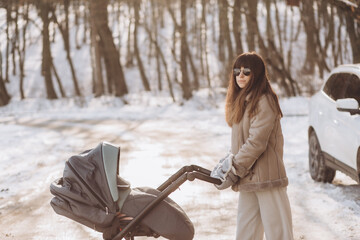 Young mother walks with a baby carriage in the park on a sunny winter day.