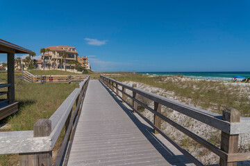 Fototapeta na wymiar Ocean and beach houses viewed from a wooden pathway in Destin Florida. Scenic coastal landscape with waterfront homes, sandy shore, sea, and blue sky on a sunny day.