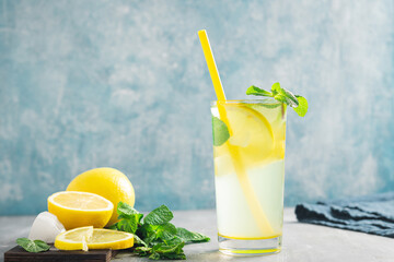 Lemonade drink or mojito cocktail in a glass with straw, lemon fruit and mint leaves, refreshing...