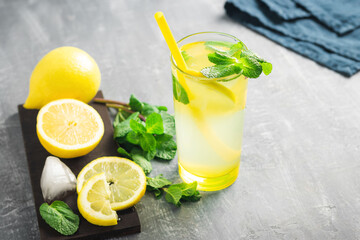 Lemonade drink or mojito cocktail in a glass with straw, lemon fruit and mint leaves, refreshing summer beverage