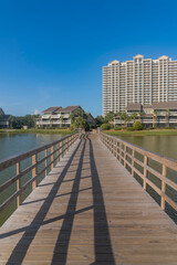 Obraz na płótnie Canvas Hotels and apartments overlooking Stewart Lake on a sunny day in Destin Florida. A wooden platform with railings and lit by sunlight is constructed over the calm water.