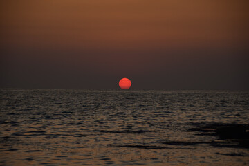 Vibrant sunset descending on the horizon, sea in golden colors, small waves gently touching the...