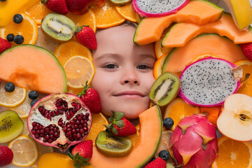 Funny child eats organic fruits. Healthy meal nutrition for children. Child eat tasty fruits. Fresh fruit and child face top view. Mix of raw fresh fruits.