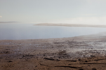 Atmospheric empty sea shore in early morning with fog above quiet water and sunlight on horizon with pebble beach and cape in haze. Zen and meditative landscape.