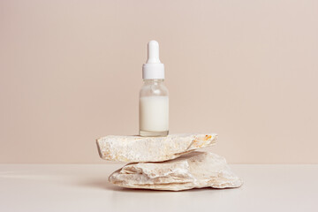 Glass dropper bottle with white liquid essence, serum or cream on stand from natural stone, beige...