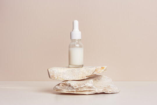 Glass dropper bottle with white liquid essence, serum or cream on stand from natural stone, beige background. Natural Organic Spa Cosmetic, minimal aesthetic mock up cosmetic skin care product