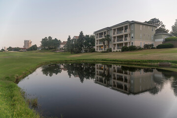Golf course with reflective pond against sky during sunset in Destin Florida. The multi-storey building with balconies is reflected in the calm water.