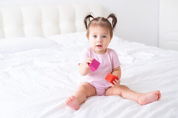 Fototapeta premium funny baby girl in pink bodysuit playing with children wooden cubes toys on bed