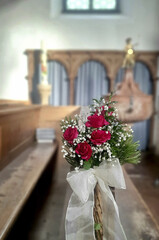 Blumenstrauß mit roten Rosen an einer Kirchenbank im Hintergrund der Kirchenraum