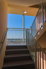 Stairwell with natural daylight from a landing with railings and outside views at Destin, Florida. Building interior open-air stairwell with wall-mounted handrail and concrete steps and landing.