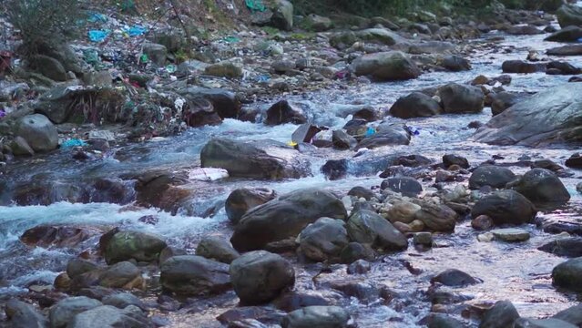 Closeup shot of river Parvati flowing in between mountains at Kasol with plastic waste around the river with some plastic waste floating in the stream. Waste dumped on side of river in Himachal. 