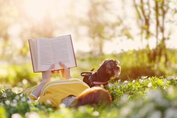 Woman with her dog lying on the blooming meadow and reading book.